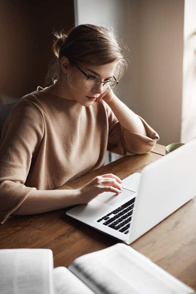 focused-good-looking-caucasian-female-entrepreneur-trendy-glasses-leaning-head-hand-gazing-laptop-screen-making-notes-notebook-book-working-hard-home-loans